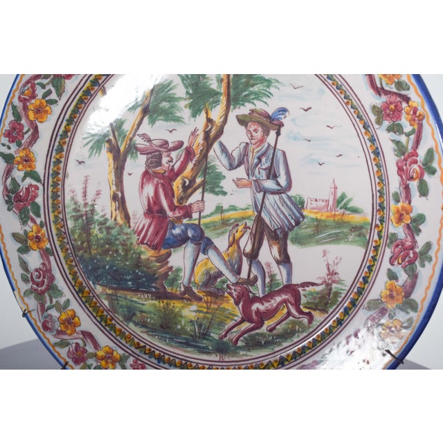 Large plate, in Portuguese Sant’Anna earthenware. Polychrome decoration with landscape and figures. In the center is a...