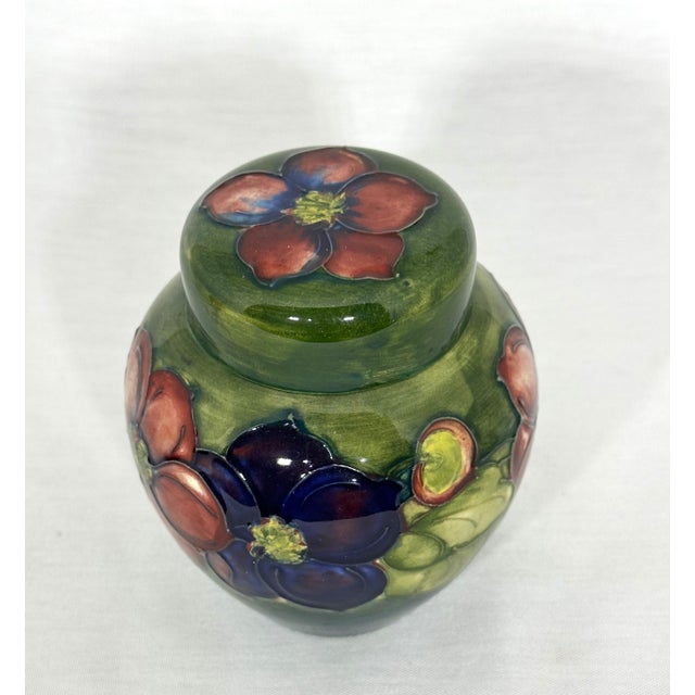 This small Moorcroft ginger jar, measuring 4" tall and 3-1/2" wide, features green glaze with vibrant clematis flower...