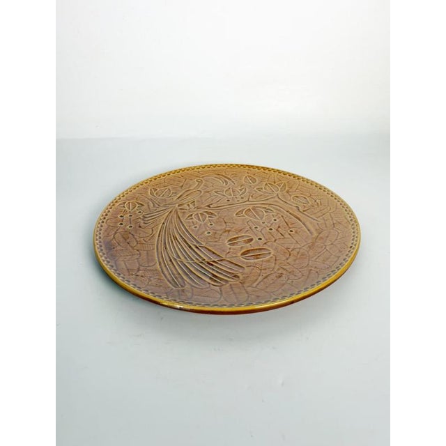Decorative round ceramic dish in a warm brown glaze, featuring a finely molded bird perched on a flowering branch...