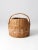 An antique hand-woven market basket featuring a distinctive pink stripe around the base and a short carrying handle. Its...