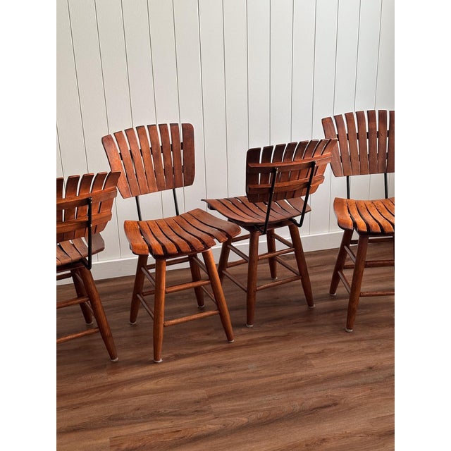 This set of four mid-century modern dining chairs features classic slatted backs and warm-toned wood with a natural, even...