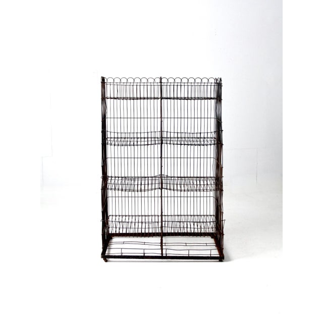 This is a vintage wire shelf rack circa early to mid 20th century. The black metal rack features four shelves with tapered...
