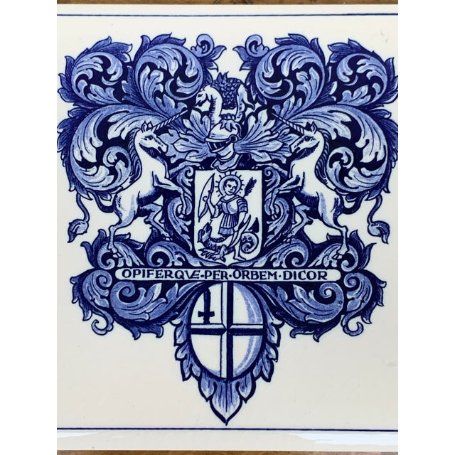 A classic Dutch Delft-style hand painted blue and white porcelain tile featuring an intricately rendered heraldic coat of...
