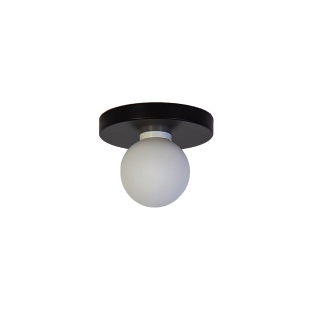 Minimal from top to bottom. This black flush mount pairs a metal base with a soft glass globe. Cool, calm, and quietly...