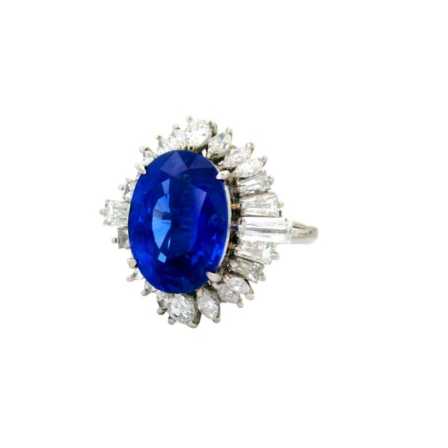 A striking ring featuring a 5.56-carat oval blue sapphire. The vibrant blue hue of the sapphire is complemented by 1.67...