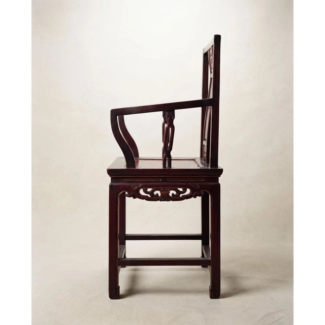 A striking pair of Chinese hardwood armchairs featuring tall open backs, shaped arms, pierced carved decoration, and...