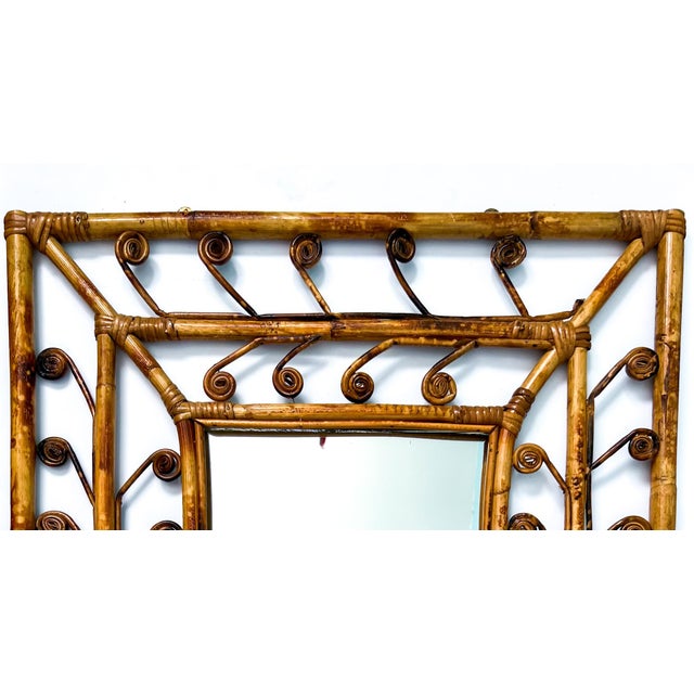 Charming vintage rattan wall mirror featuring intricate curled cane accents and a warm, honey-toned finish. Likely crafted...