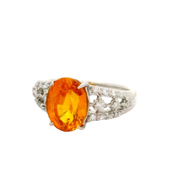 A striking ring featuring a 3.67-carat oval orange sapphire. The vibrant orange hue of the sapphire is complemented by...