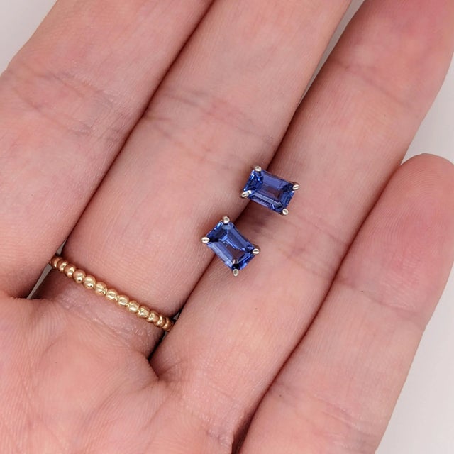 These elegant earrings feature emerald cut tanzanite stones, exuding a captivating violet-blue hue. The stones are...