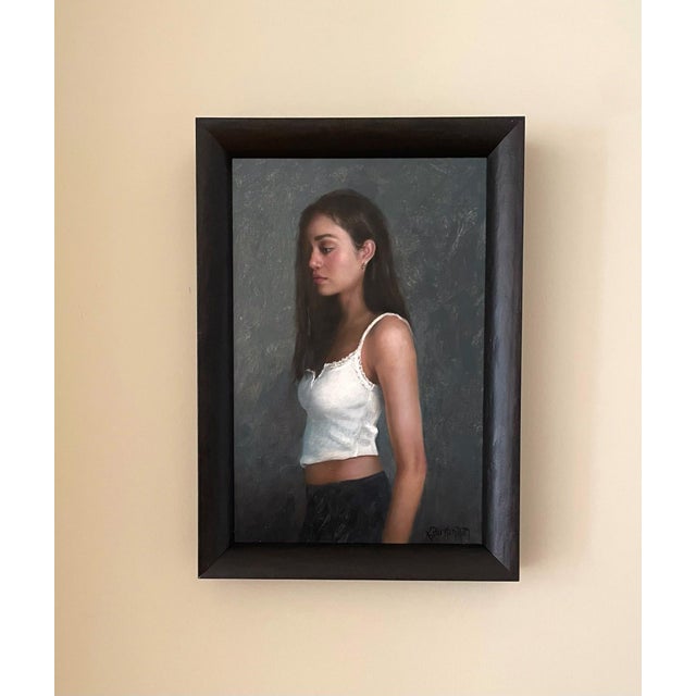 In "Jules," a young woman stands in profile, her expression contemplative against a softly textured gray background. The...