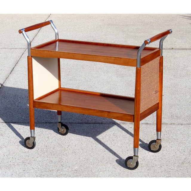 Beautiful vintage Mid-Century Modern rolling bar cart featuring warm teak wood shelves, elegant chrome accents, and...