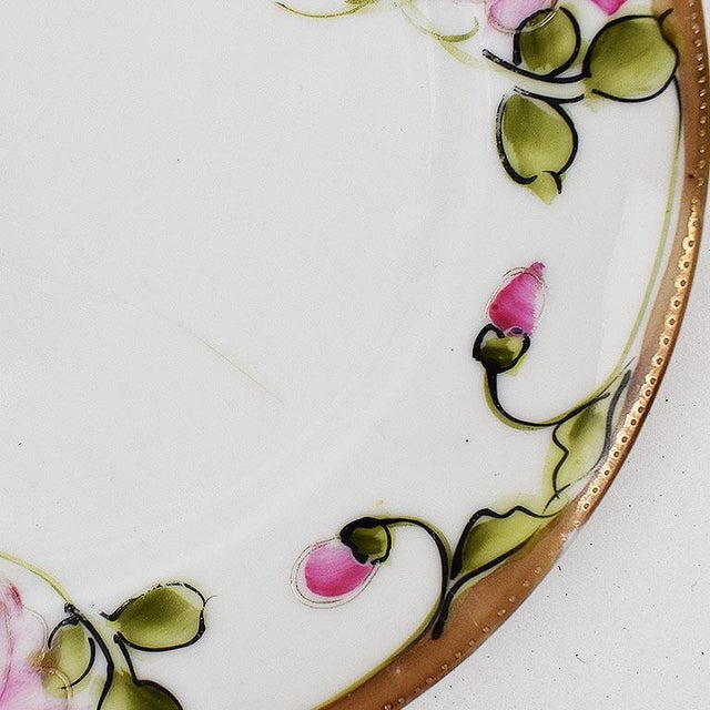 A small round ceramic plate with a pink and green floral design around the edges. The center of the plate is a crisp white...