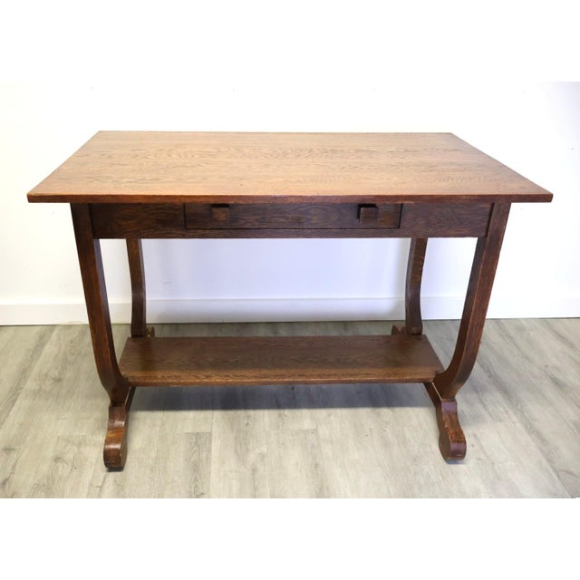 Early 20th-century Arts & Crafts oak library table featuring distinctive lyre-form side supports, a single drawer with...