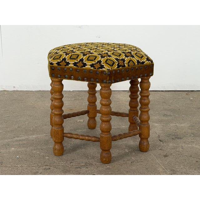 A solid oak bobbin-turned stool with geometric needlepoint upholstered seat, Danish workshop production, 1950s. The seat...