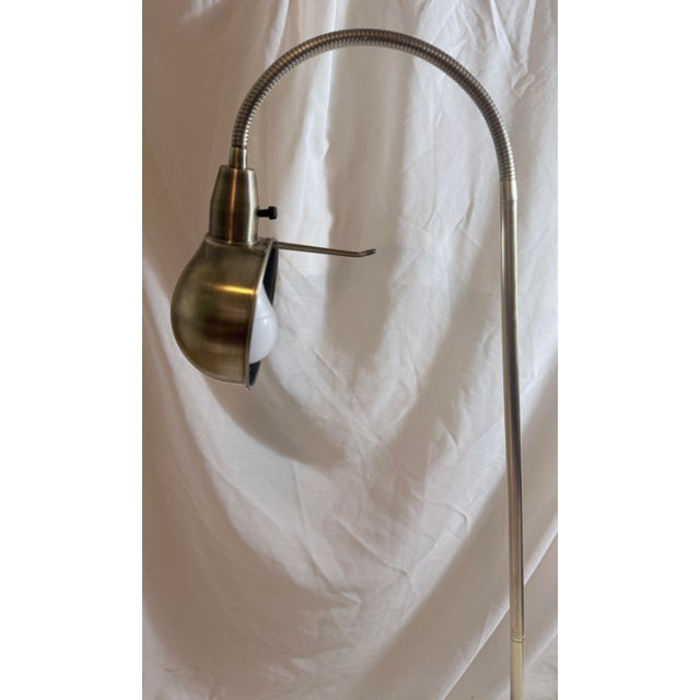 A classic vintage brushed brass pharmacy-style floor lamp featuring an adjustable gooseneck arm and directional dome...
