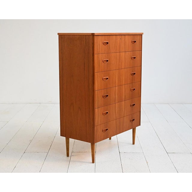 Teak chest of drawers with six front drawers, integrated carved handles, and tapered solid wood legs. Scandinavian...