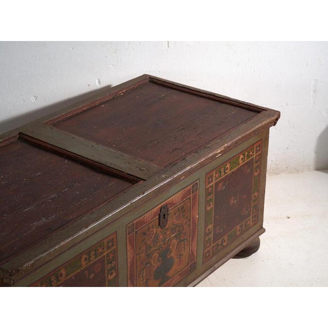 This antique painted dowry chest in pine is a polychrome folk trunk with a flat lid and a decorated front, on bun feet. It...