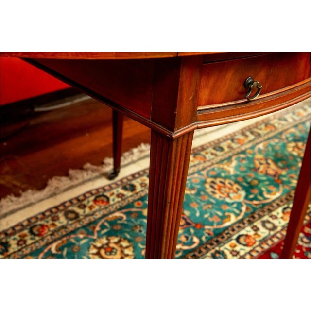 Flame mahogany oval Pembroke table with banded inlay, tapered square legs and original brass pulls and casters. This is a...