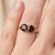 Exude a grounded, sophisticated elegance with this captivating 18k gold-plated two-stone ring. Featuring a pair of...
