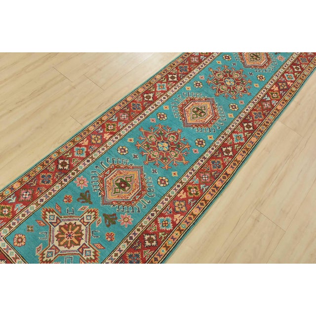 A tribal Caucasian Kazak runner hand-knotted with fine wool on a cotton foundation. This rug features a row of geometric...