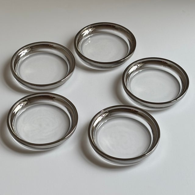 A sophisticated set of five vintage clear glass coasters featuring elegant silver-toned metal rims in the iconic style of...