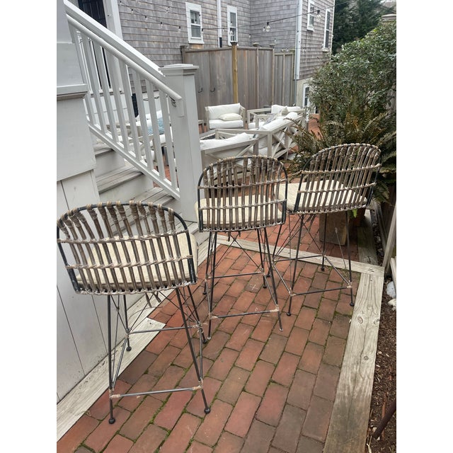 Sculptural set of three iron bar stools featuring airy, architectural bases and hand-wrapped woven seats and backs. The...