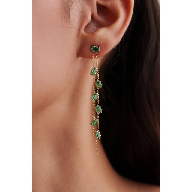 These long drop chain earrings feature a 3.25 ct rectangular-cut natural emerald, set in 14k yellow gold. Each emerald...