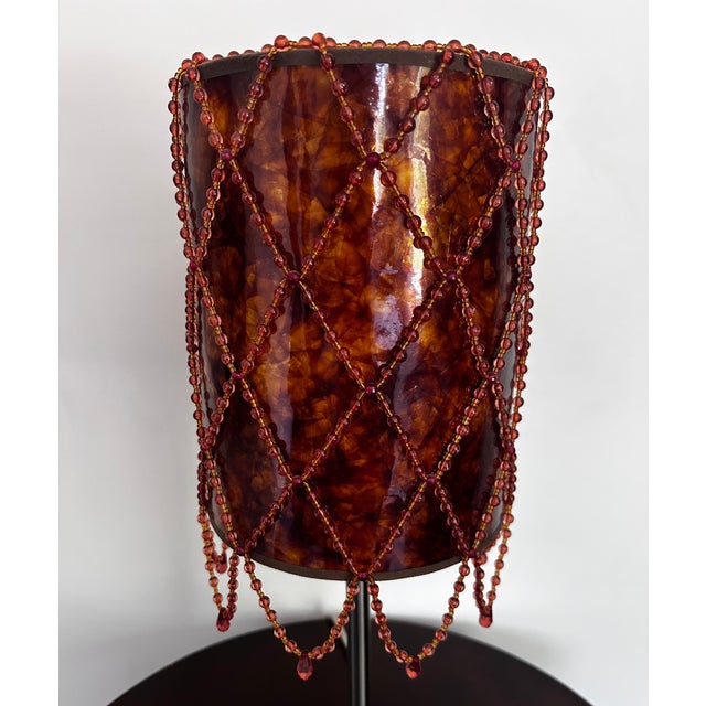 This unique lamp shade features a warm mica-style cylindrical shade accented with draped red beaded fringe for a glamorous...