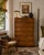 A beautifully crafted 1970s John Widdicomb Campaign-style highboy dresser featuring striking burled wood veneers with rich...