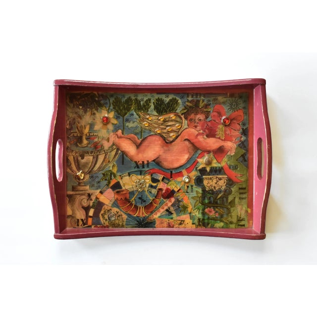 A vintage, puce pink serving tray, decoupaged and lacquered with a colorful illustration featuring a cupid, a fountain,...