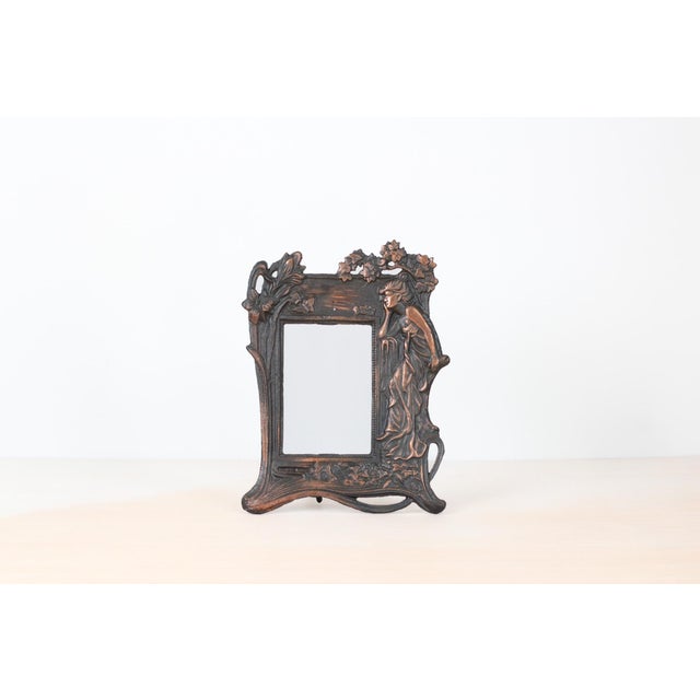 Decorative cast iron picture frame featuring an Art Nouveau–inspired female figure framed by flowing botanical motifs....