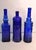 A striking collection of three vintage cobalt blue art glass bottles featuring distinct architectural forms, embossed...