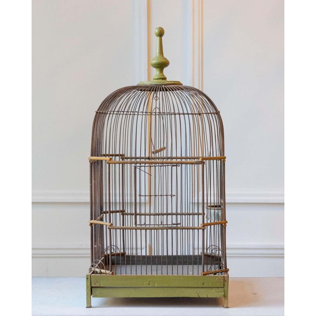 A late 19th-century birdcage featuring a charming wooden structure with a soft green-painted base and a turned wood finial...