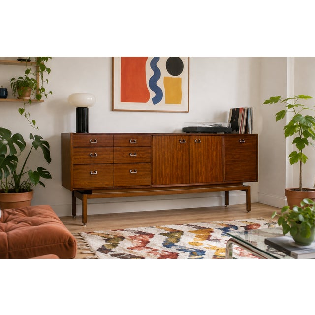 A1960s Tola sideboard by Nathan, featuring three wide drawers, a shelved double cupboard and a drop-down cupboard to the...