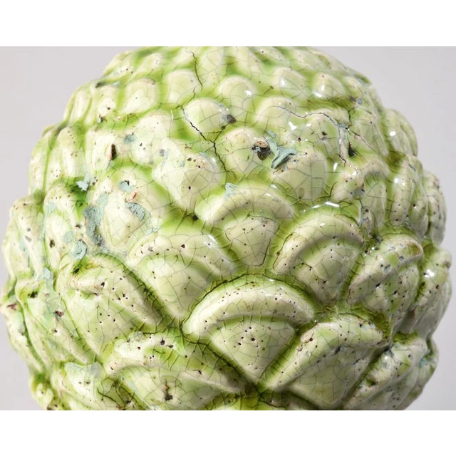 A sculptural ceramic artichoke finial in a pale celadon glaze with subtle crackle and speckled surface. The classical...