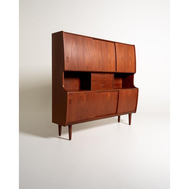 Danish teak highboard from the 1960s, with sliding doors, four drawers, pull-out trays, and a bar with a decorated mirror....