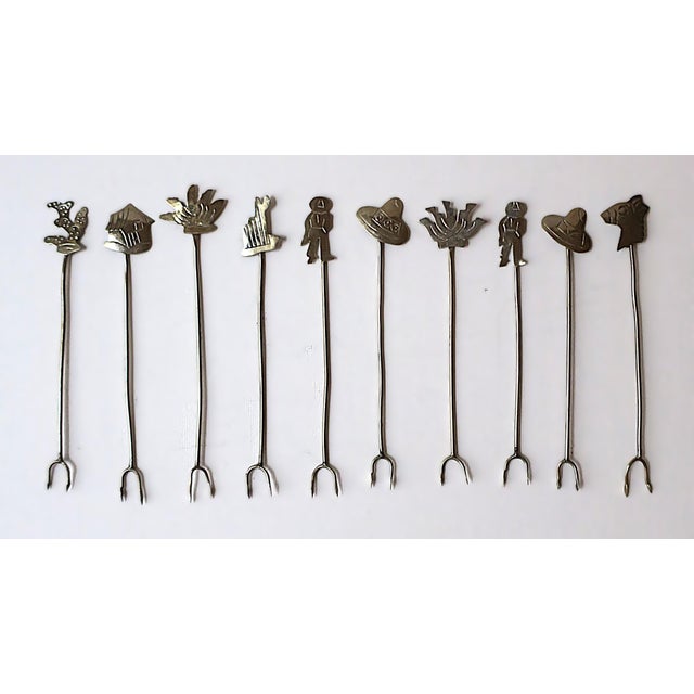 A set of ten (10) Mexican hand-crafted alpaca metal cocktail or appetizer forks/picks with charm tops, circa mid-20th...