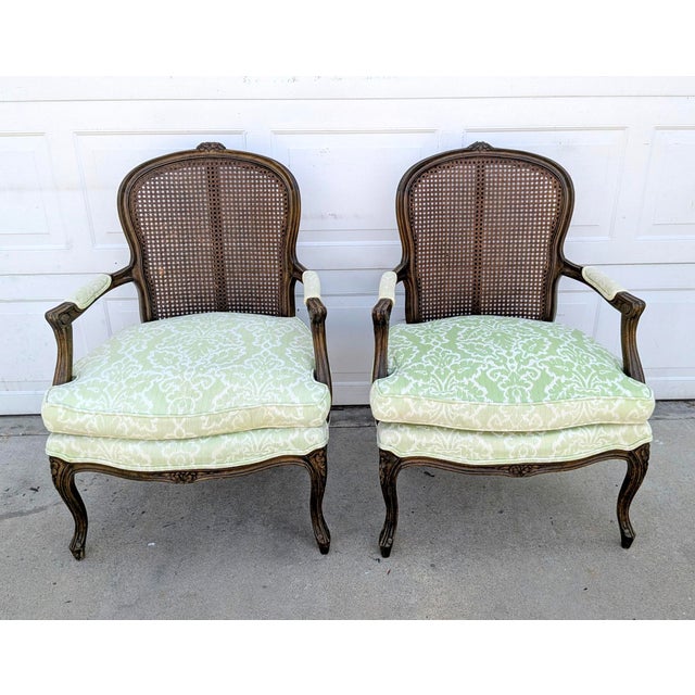 A beautiful pair of vintage French Louis XV–style bergère armchairs featuring gracefully shaped exposed wood frames,...