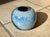 Handcrafted ceramic spherical vase with a striking blue-gray flowing glaze and a glossy finish on a light-colored body....