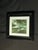 Elegant black and white framed landscape photograph featuring a small boat, tree, shoreline, and dramatic outdoor scenery....