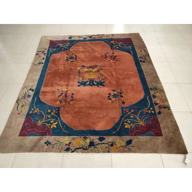 A four lobed, nearly open, apricot field is centered on a vase on stand with flowering bouquet, rocks and more flowers...