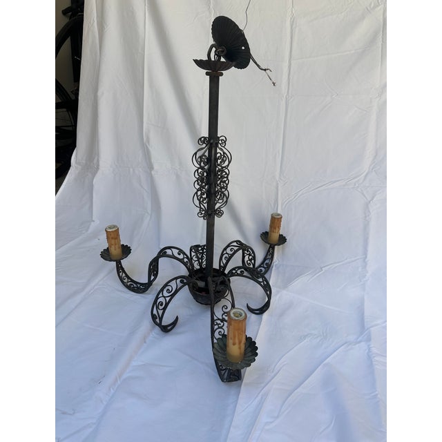 Three-arm black wrought iron chandelier with dense scrollwork on arms and center column; scalloped bobeches, drip candle...
