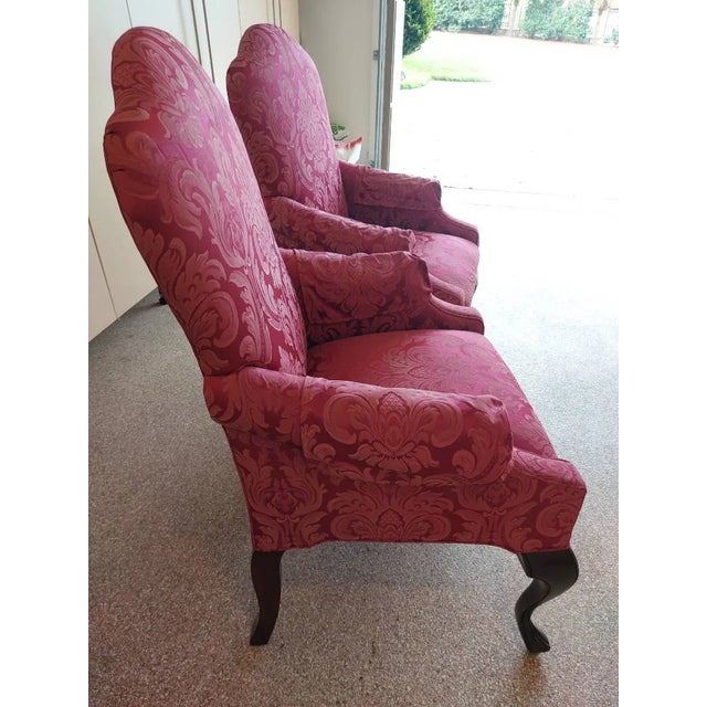 Pair of traditional burgundy Queen Anne-style upholstered armchairs featuring dark wood cabriolet legs and a rose/crimson...