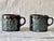 A pair of black Tenmoku glazed mugs with potter Eric Moore's signature XO design. Each mug holds 12 ounces and is food...