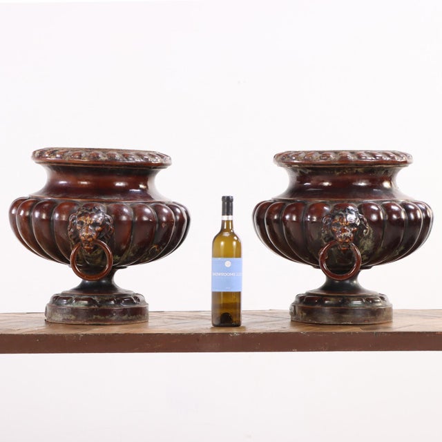 Here is a gorgeous pair of enameled garden urns featuring lion-mask ringed handles. The deep understated reddish-brown...