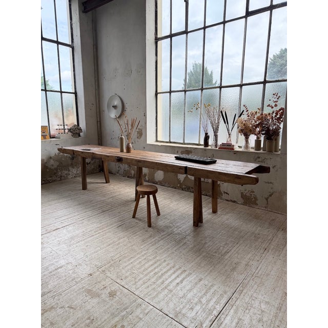 An antique, large-format table with a workbench-style top and a brutalist or folk art base. the top, likely from a very...