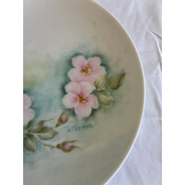 A charming set of two vintage hand-painted floral plates, each signed by the artist and featuring soft pastel botanical...