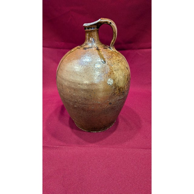 This hand-thrown 19th-century stoneware whiskey jug features a prominent ovoid body and a single pulled loop handle. The...