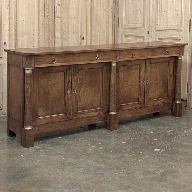 Early 19th Century French Empire Period Walnut Grand Buffet was meticulously hand-crafted by skilled artisans who drew...