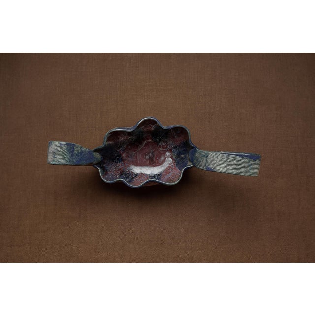 A sculptural centerpiece bowl with fluted body and dramatic double loop handles. Finished in an iridescent glaze of jewel-...